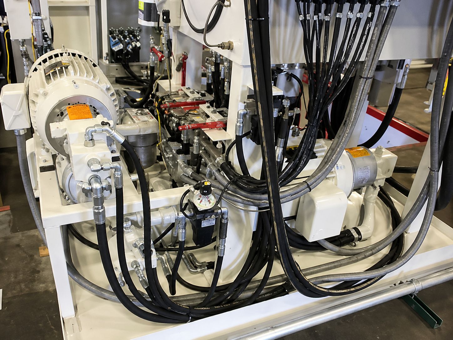 Close-up of a complex hydraulic system with various hoses, pipes, and valves on a metal framework. The setup appears industrial and technical.